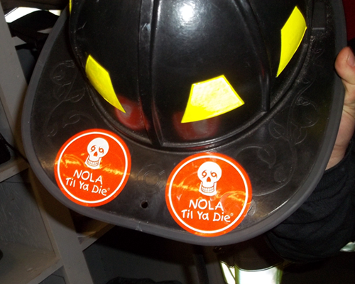 Fire helmet with Nola Til Ya Die orange stickers and a person holding it in New York.