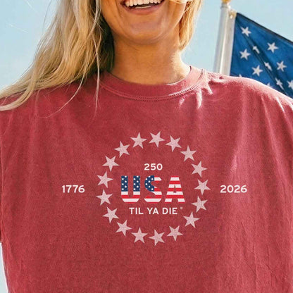 Person wearing a red t-shirt with special 250th USA Til Ya Die graphic, sitting on a red truck by the beach.