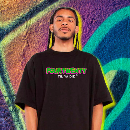Person wearing a black t-shirt with colorful text - Four Twenty Til Ya Die - against a vibrant graffiti wall.
