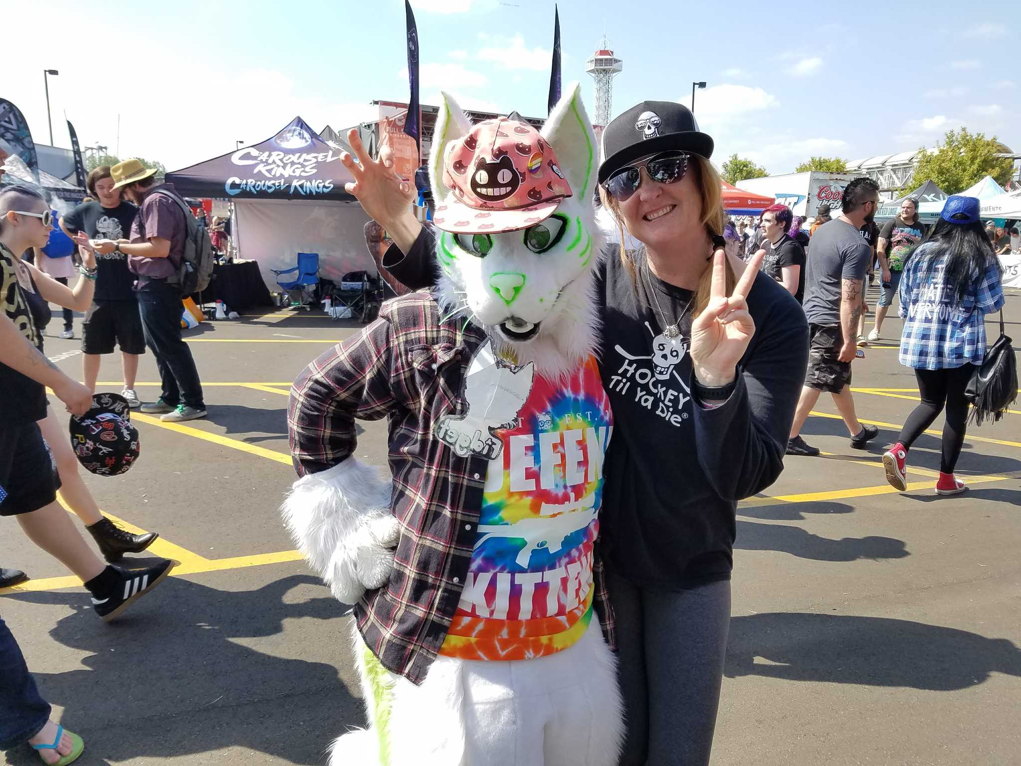 Person in a colorful costume at Vans Warped Tour and another with a Hockey Til Ya Die shirt from Nola Til Ya Die with a black cap and sunglasses posing at the festival.